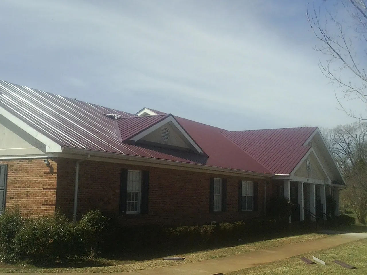 Red metal roof with gabled entries on a long brick building, from a Hail Damage Roof Repair job in Grant